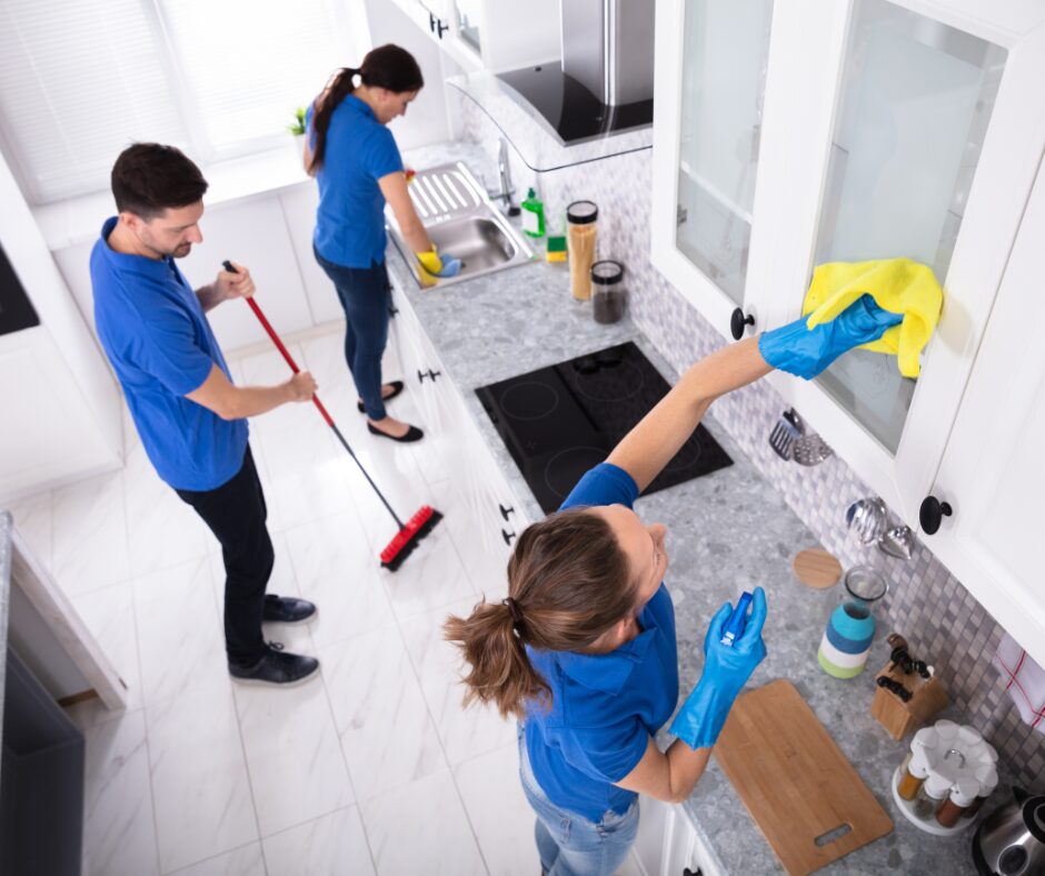 Professional cleaners completing a move-out cleaning in a kitchen, wiping cabinets and cleaning floors before final inspection